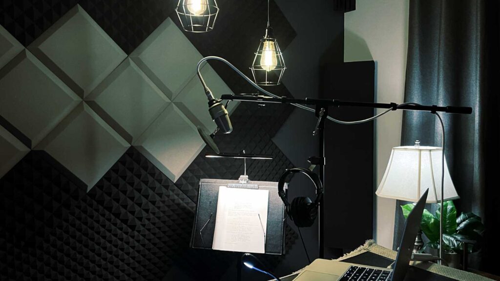 A cozy recording studio featuring a microphone, headphones, sheet music on a stand, and soft lighting from pendant lamps and a table lamp.